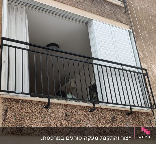 מעקה מתכת שחור על מרפסת עם תריסים פתוחים